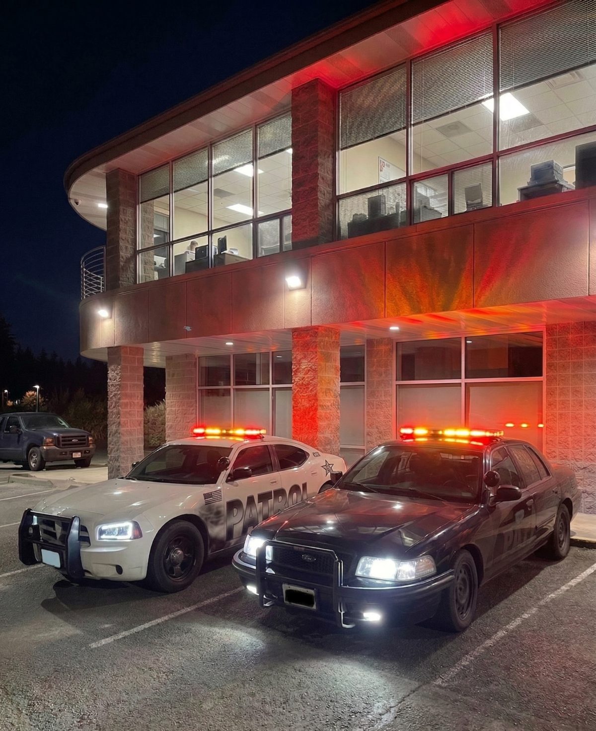 Two American Patrol LLC patrol cars with lights on outside the company office in Everett, WA, at night